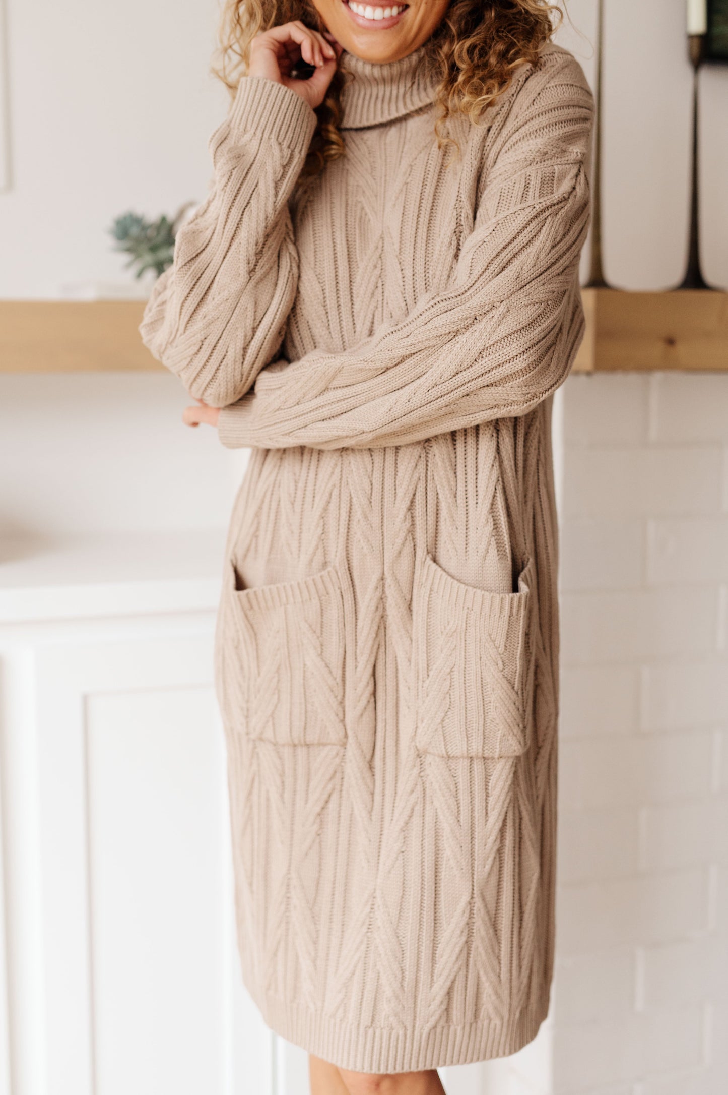 Woman wearing a beige cable knit dress with a turtleneck in a neutral setting