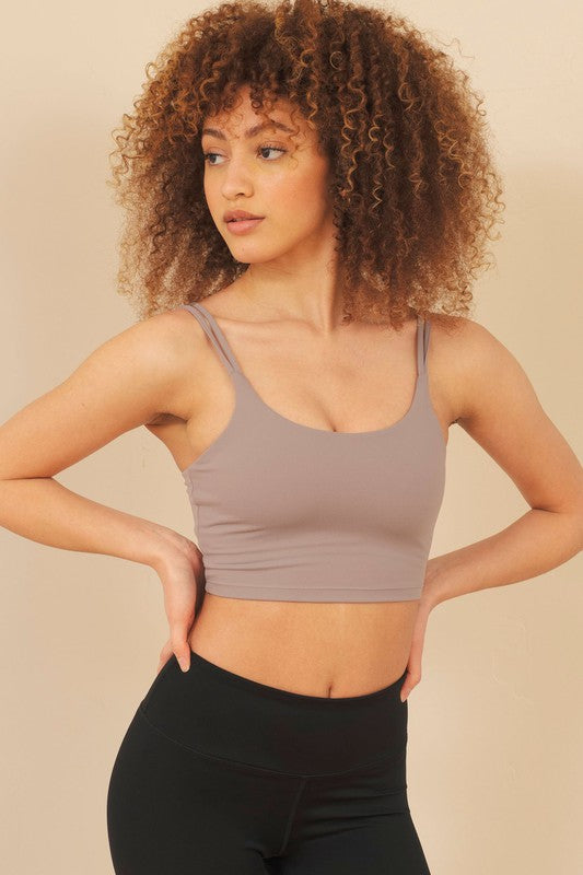 Woman wearing a beige sports bra and black leggings against a beige background