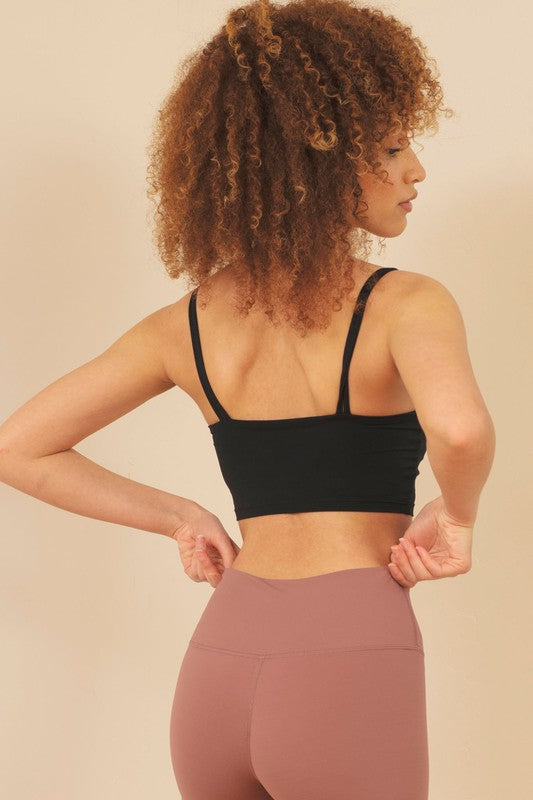 Woman wearing a black sports bra and pink leggings against a beige background