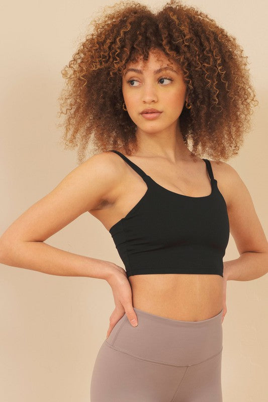 Woman wearing a black sports bra and gray leggings against a beige background