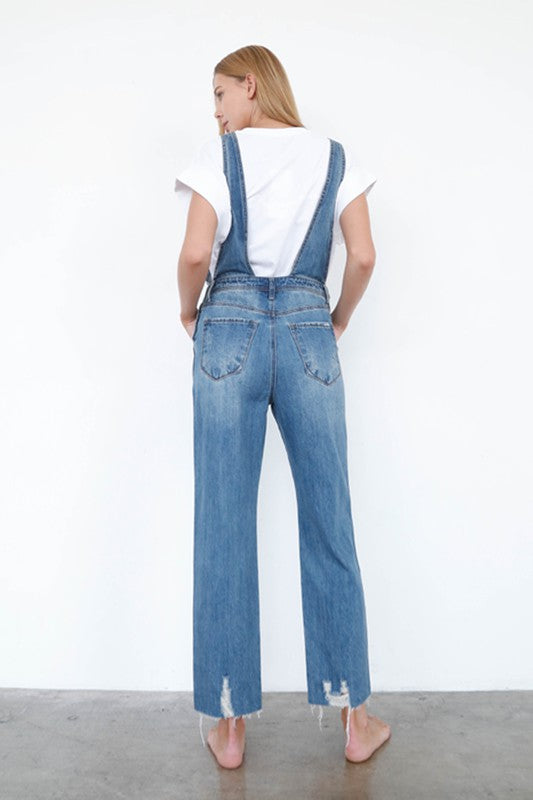 Person wearing blue denim overalls with a white background