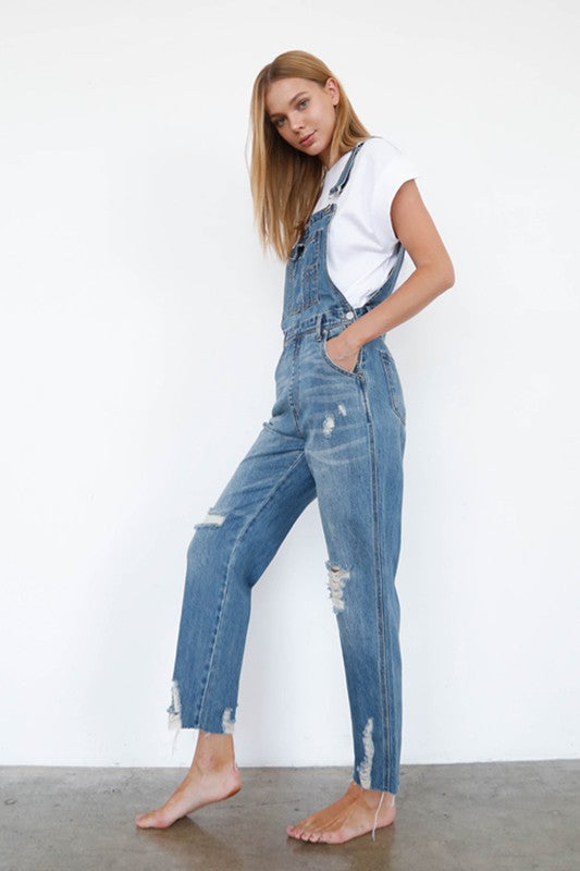 Woman wearing a denim overalls with a white top against a plain background