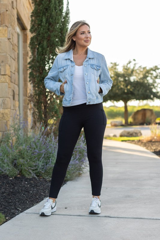 Woman wearing a denim jacket, white shirt, and black leggings walking outdoors.