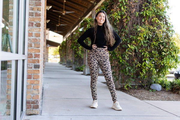 Person wearing a black top and patterned pants standing on a sidewalk.