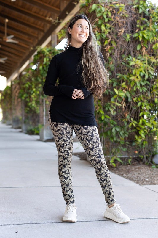 Woman wearing a black top and patterned leggings standing outdoors on a pathway.