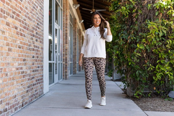 Woman in a white shirt and patterned leggings standing on a sidewalk next to a brick building.