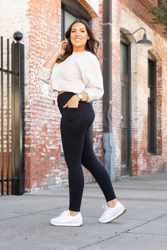 Woman wearing a white sweater and black leggings standing in front of a brick building.