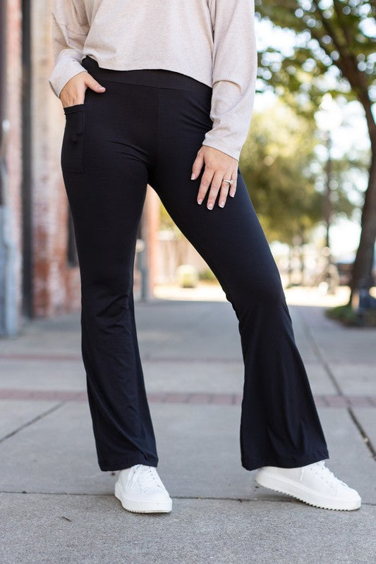Person wearing black flared pants and white sneakers on a sidewalk.