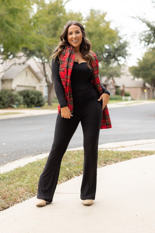 Woman wearing a black outfit with a red plaid vest on a sidewalk.