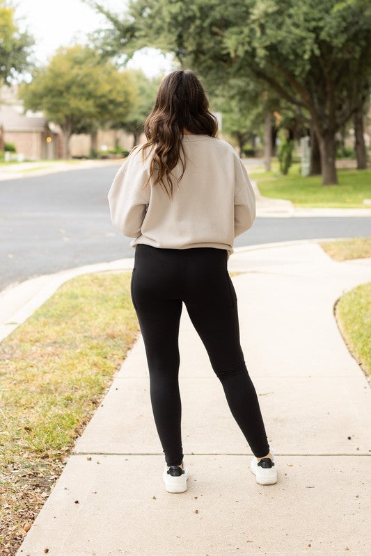 Person wearing a beige sweater and black leggings walking on a sidewalk.