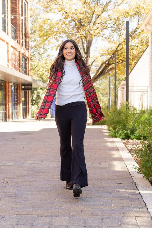 Woman walking outdoors on a sidewalk with a red plaid shirt and black pants.