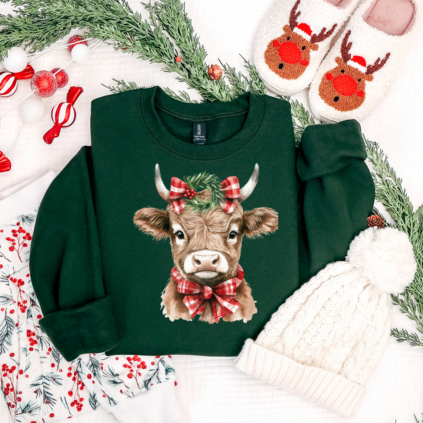 Green sweatshirt with a cow design wearing a red bow, surrounded by Christmas decorations.