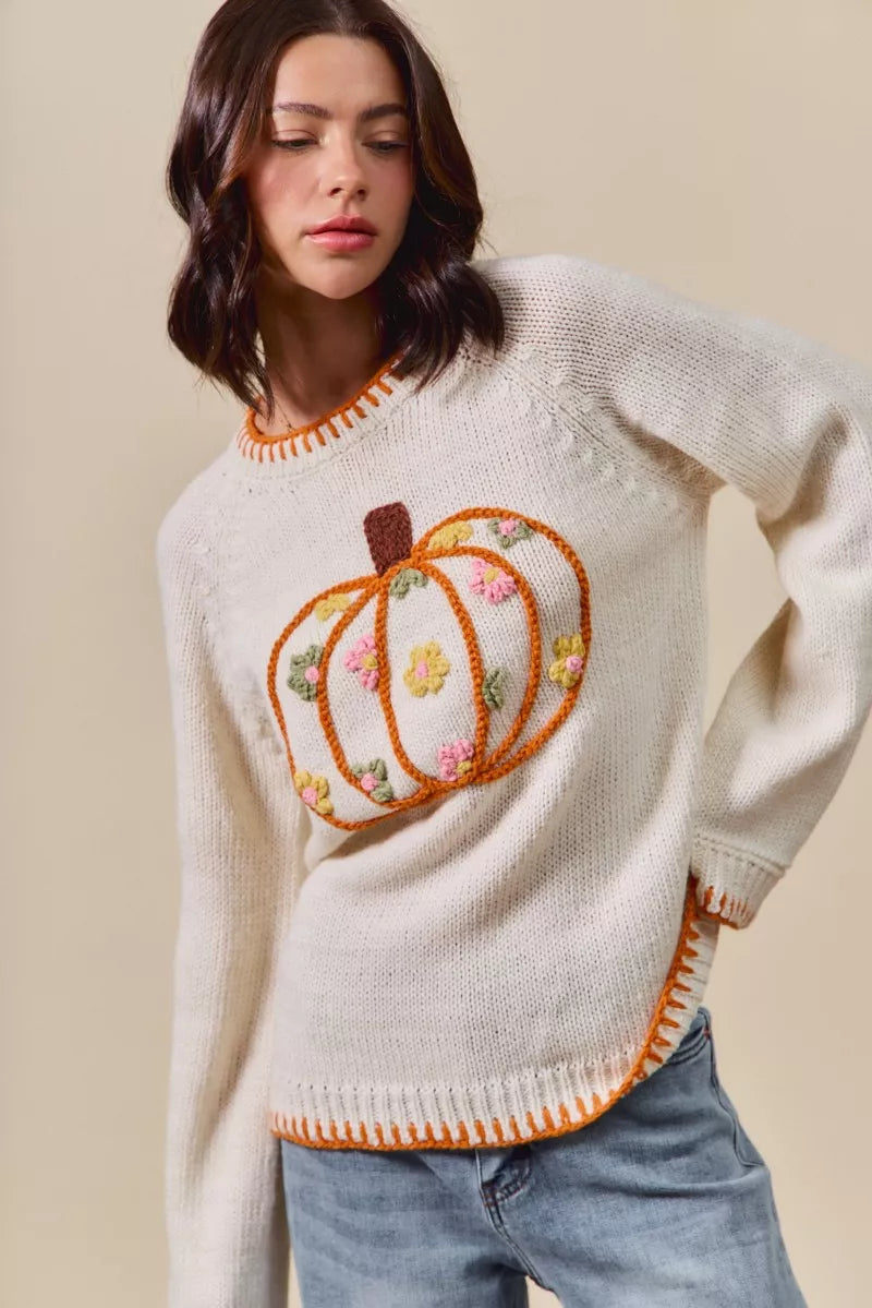 Woman wearing a cream sweater with a pumpkin design on a beige background