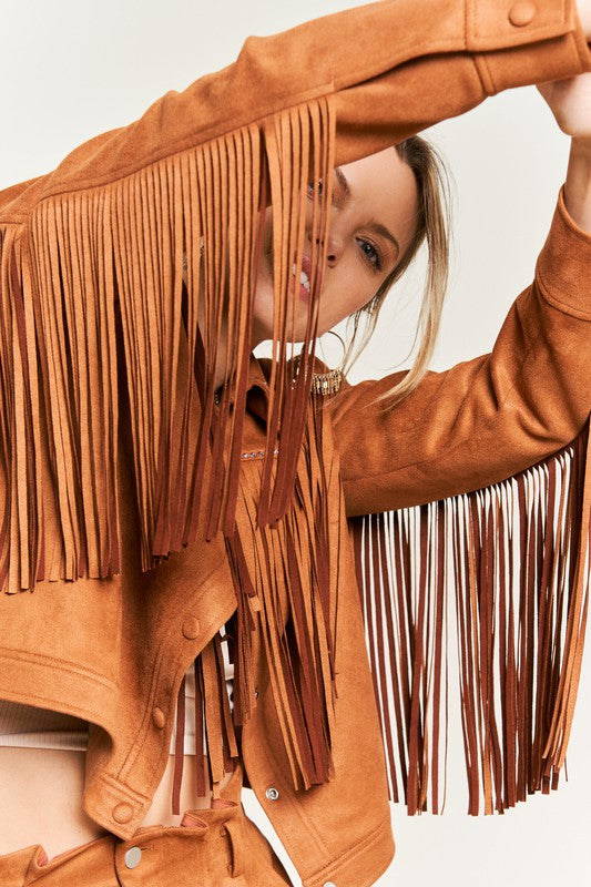 Person wearing a brown suede jacket with fringe details on a plain background