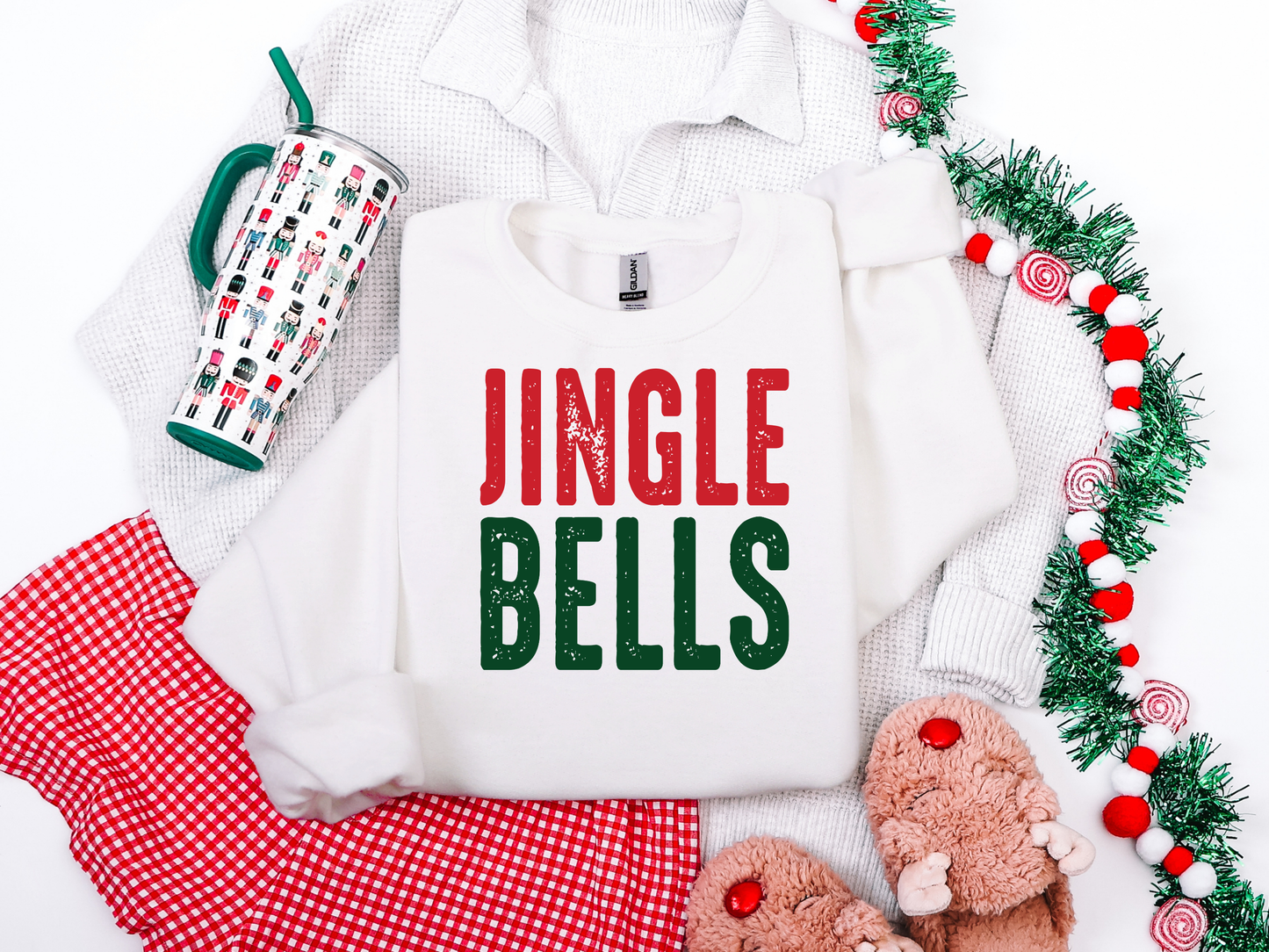 White sweatshirt with 'Jingle Bells' text, mug, red pants, and festive decor on a white background