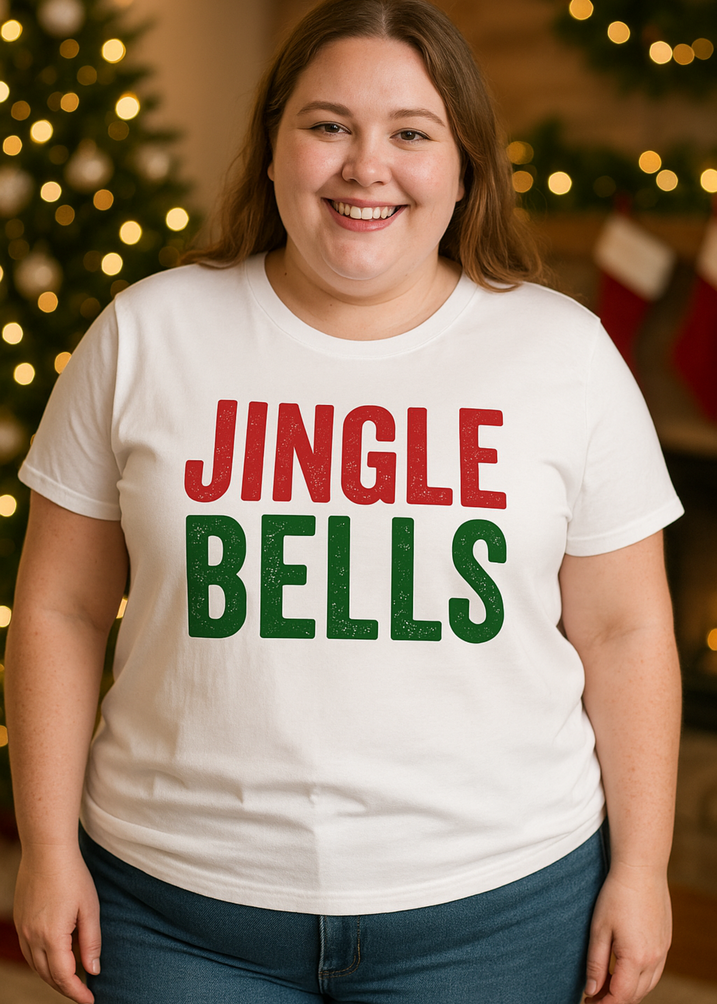 Person wearing a white t-shirt with 'JINGLE BELLS' text in red and green, standing in front of a Christmas tree and stockings.