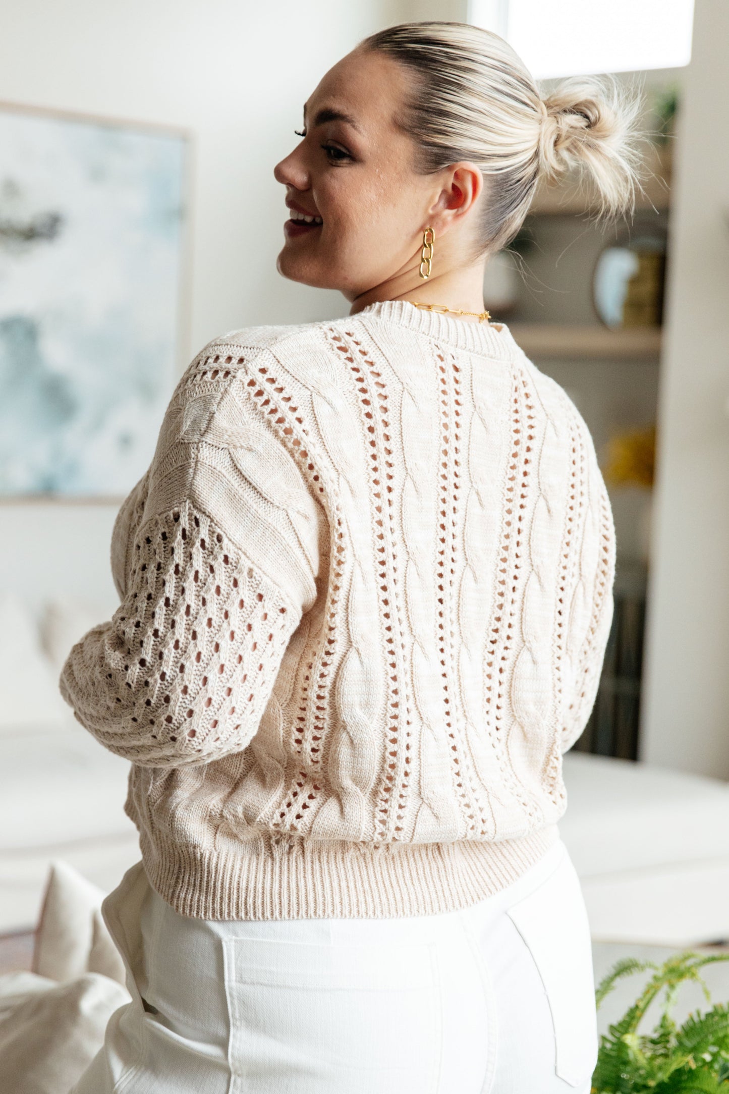 Woman wearing a beige cable knit sweater in a home setting