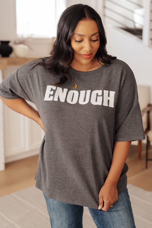 Woman wearing a gray t-shirt with 'ENOUGH' printed on it in a home setting.