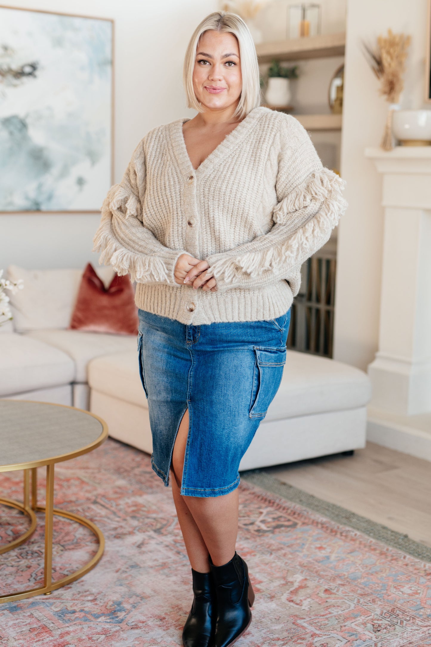 Woman wearing a beige cardigan and blue denim skirt in a living room setting.