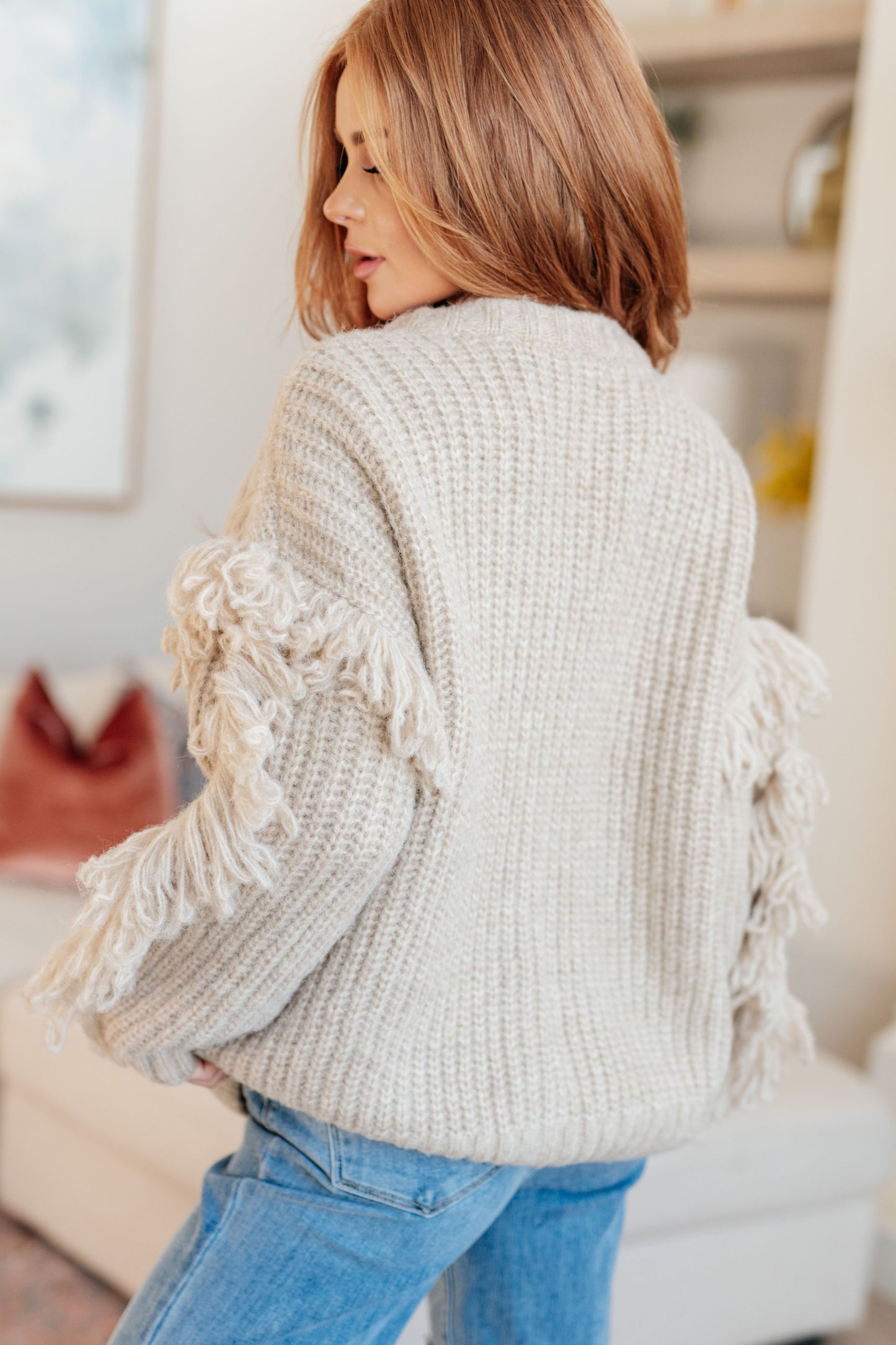 Woman wearing a beige knitted cardigan with tassels in an indoor setting