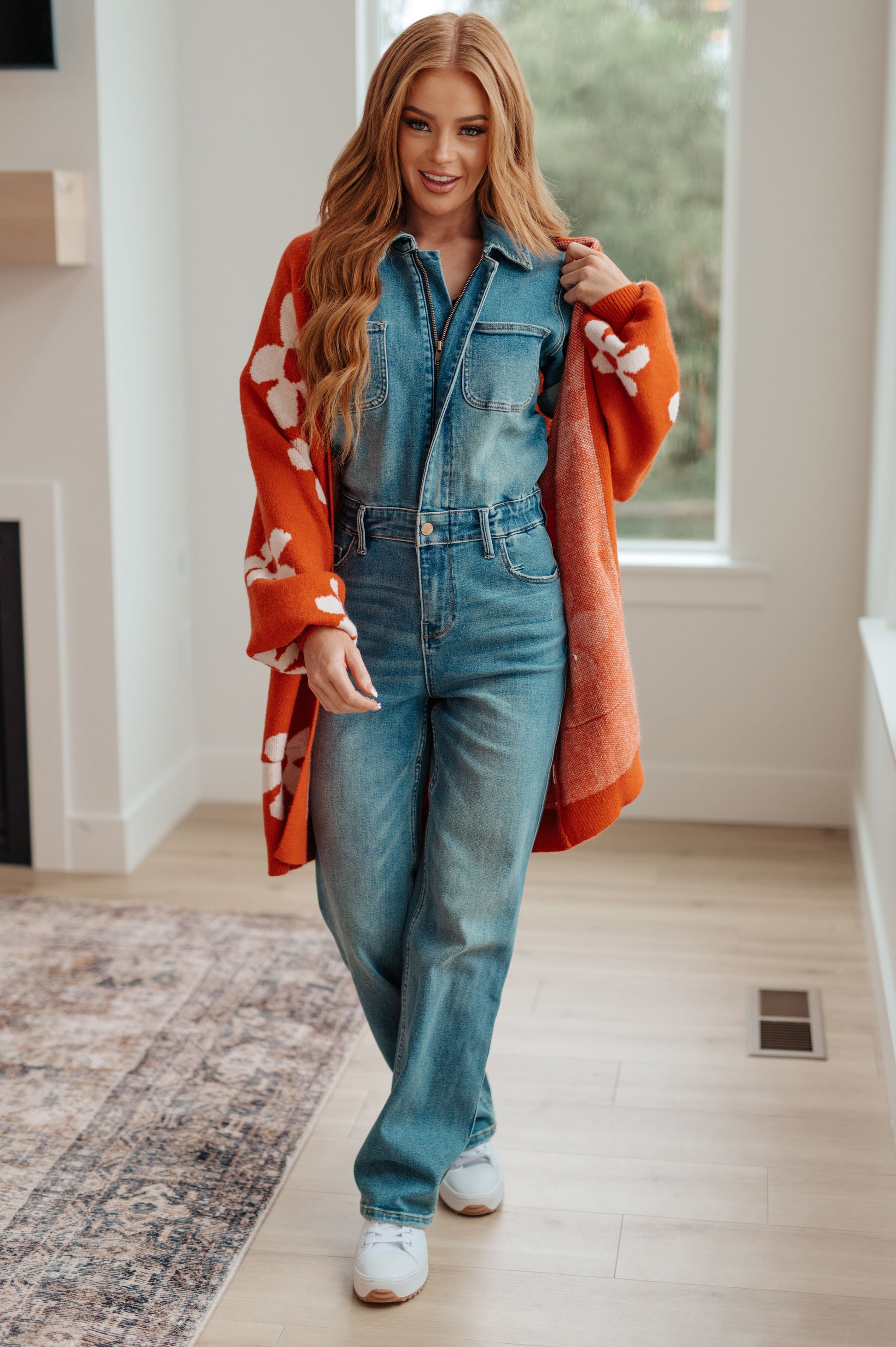 Woman wearing a denim jumpsuit with an orange patterned shawl indoors.
