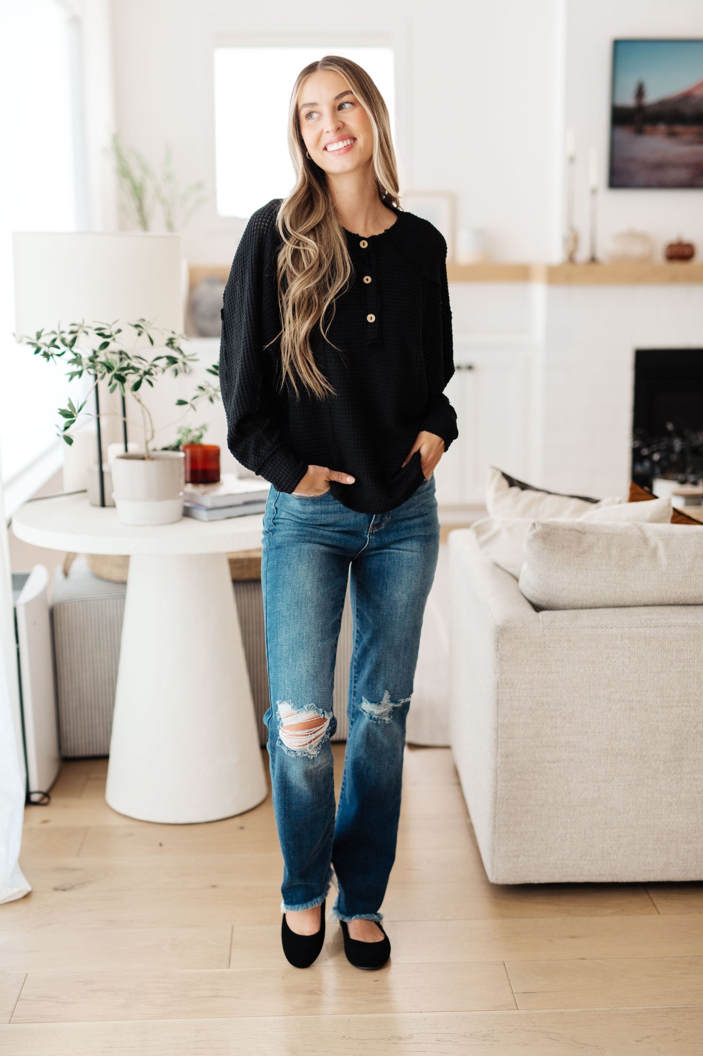 Woman in black sweater and blue jeans standing in a modern living room.