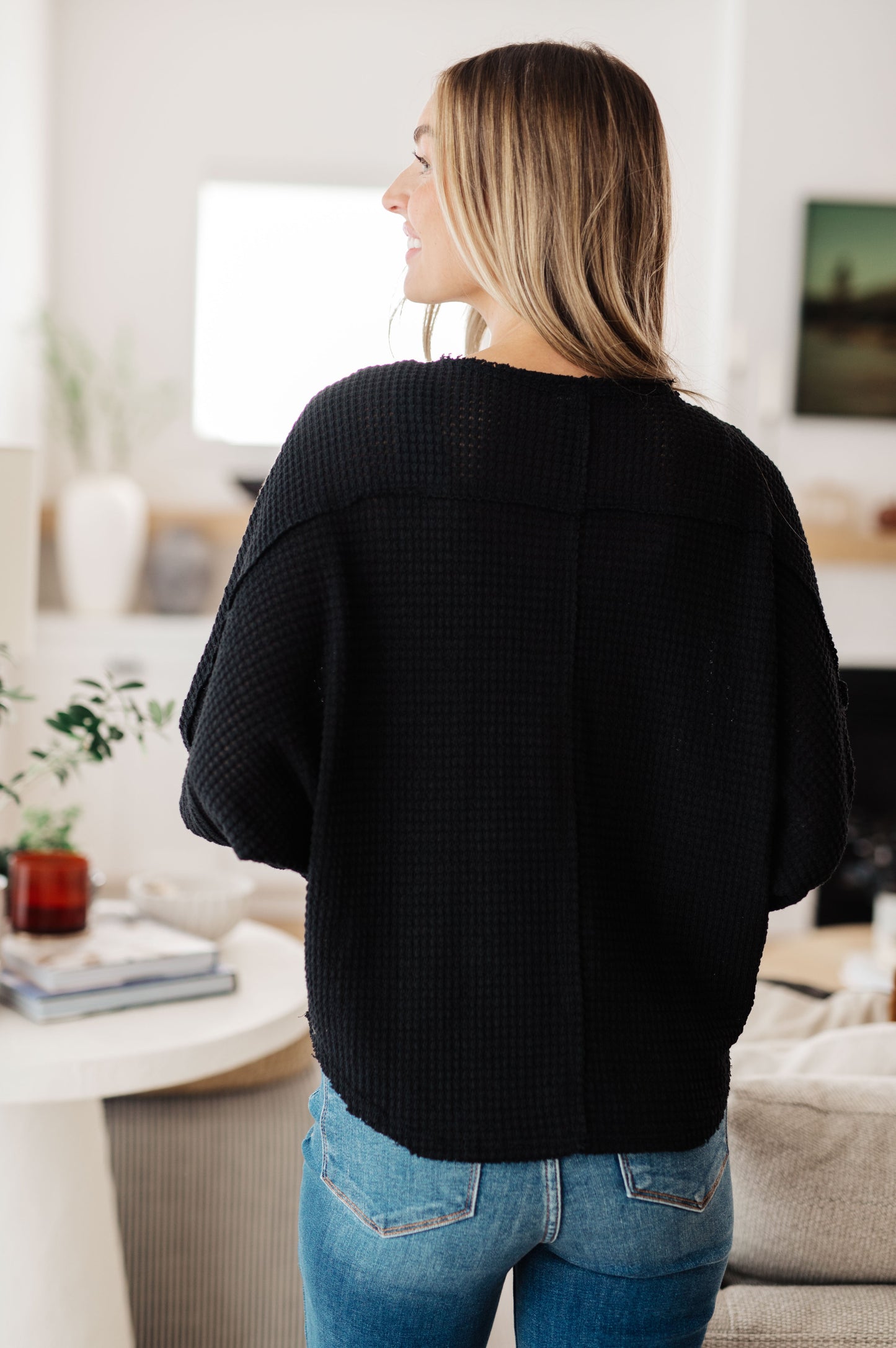 Person wearing a black sweater and blue jeans in a living room setting