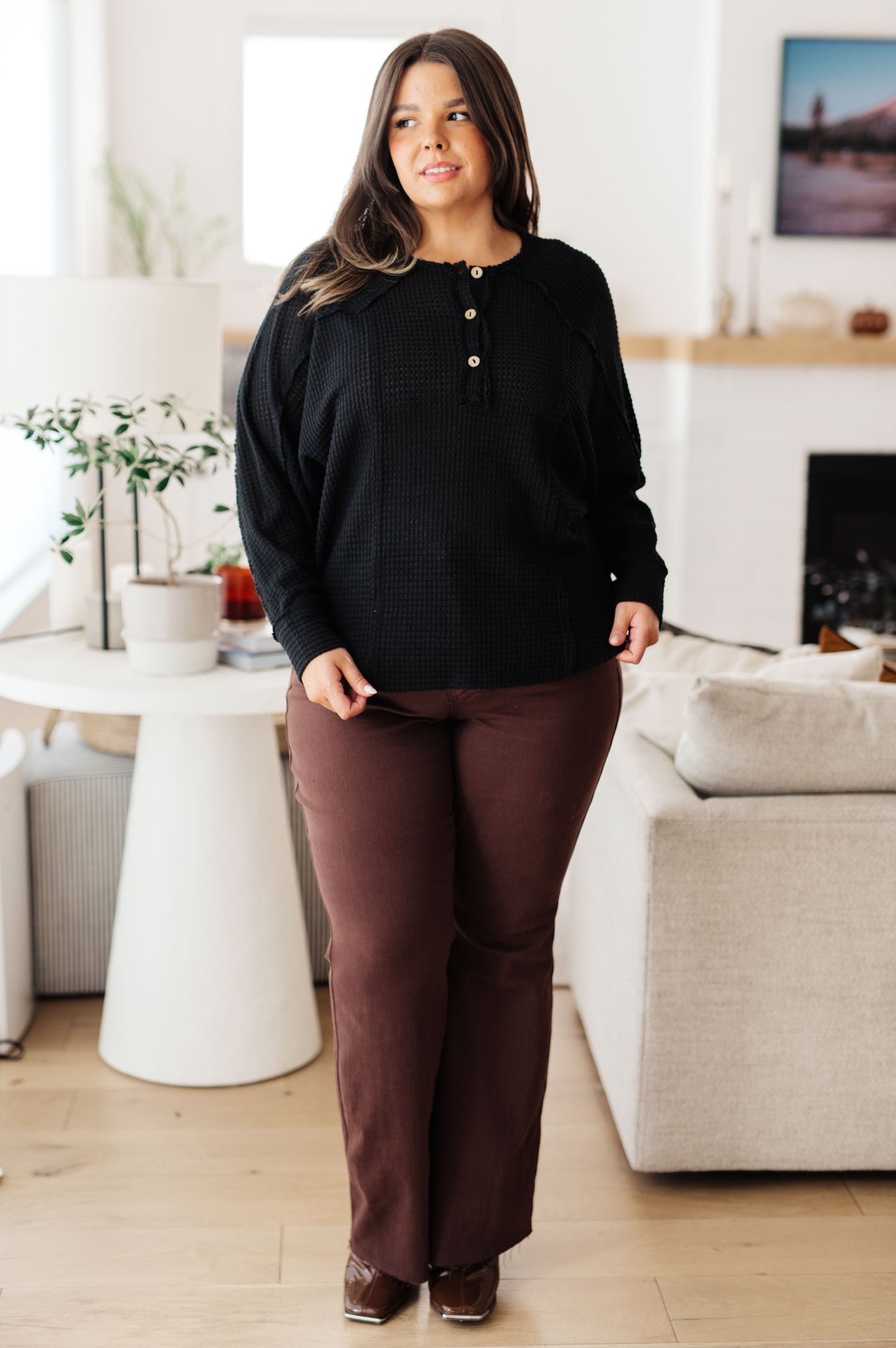 Woman in a black top and brown pants standing in a living room.