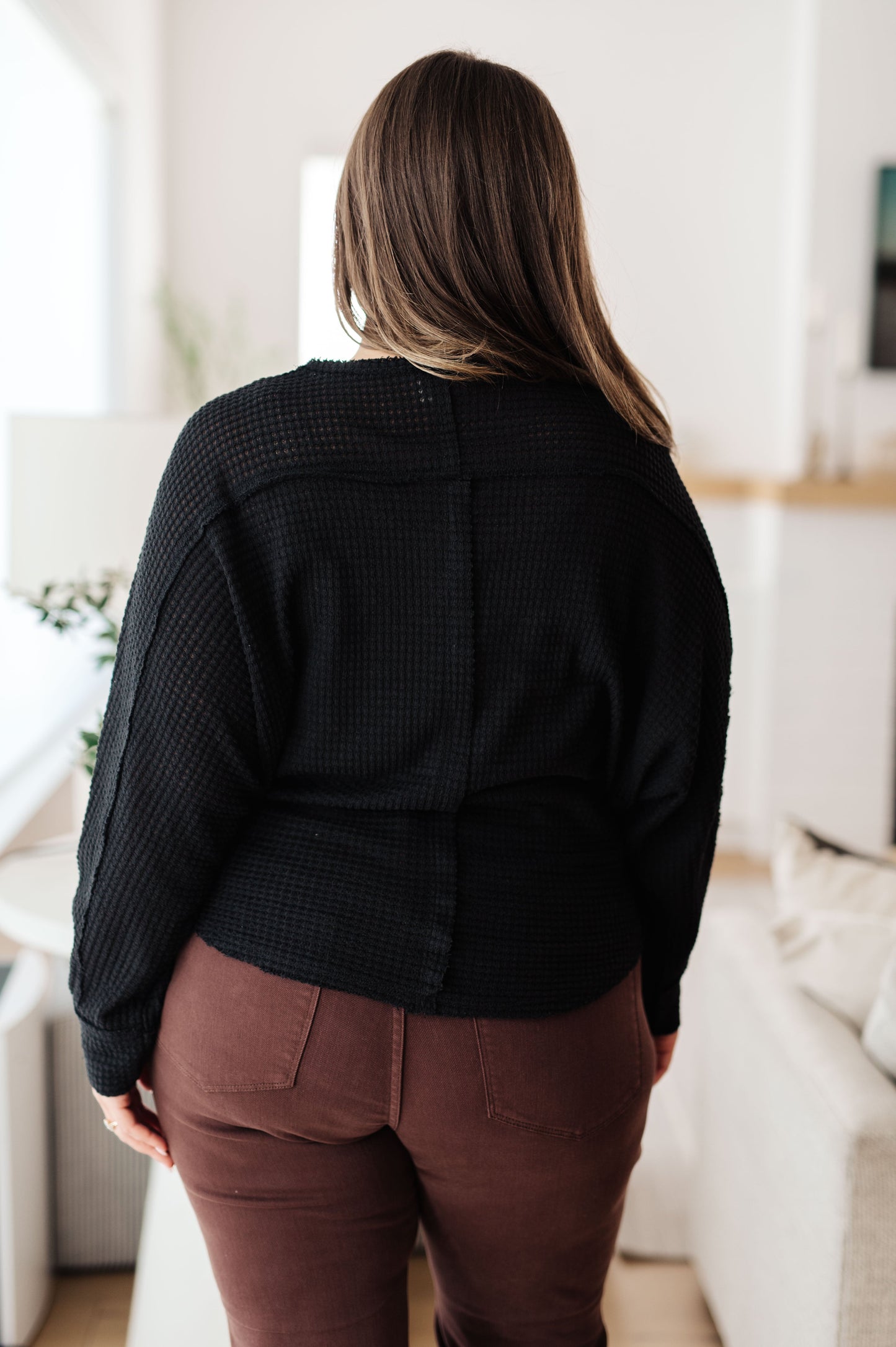 Person wearing a black jacket and brown pants in a room with white walls and furniture.