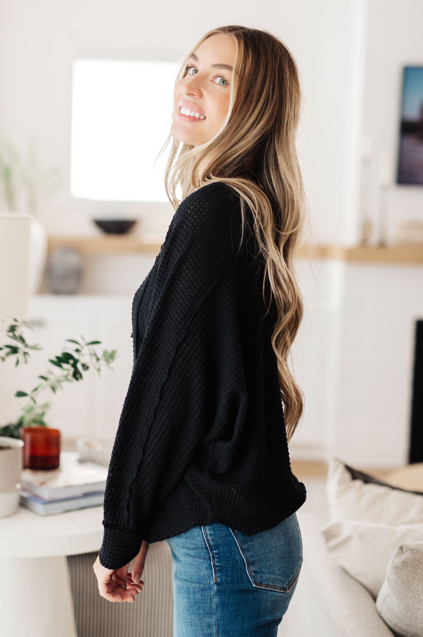 Woman wearing a black sweater and blue jeans in a living room setting