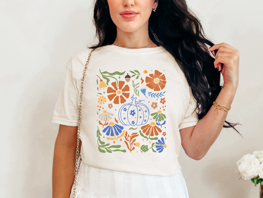 Woman wearing a white t-shirt with colorful floral and pumpkin design against a plain background