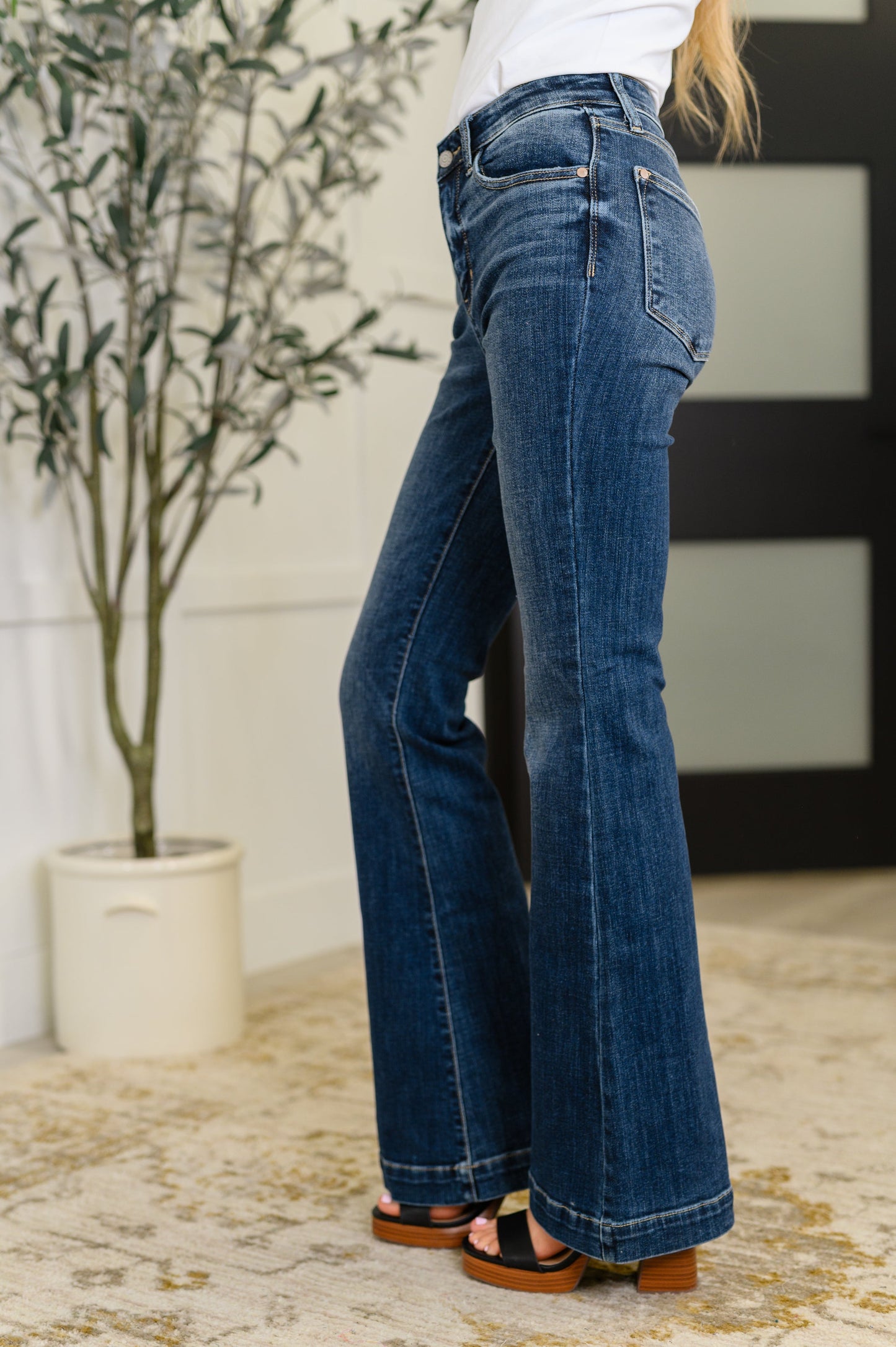 Person wearing blue jeans standing indoors with a plant in the background