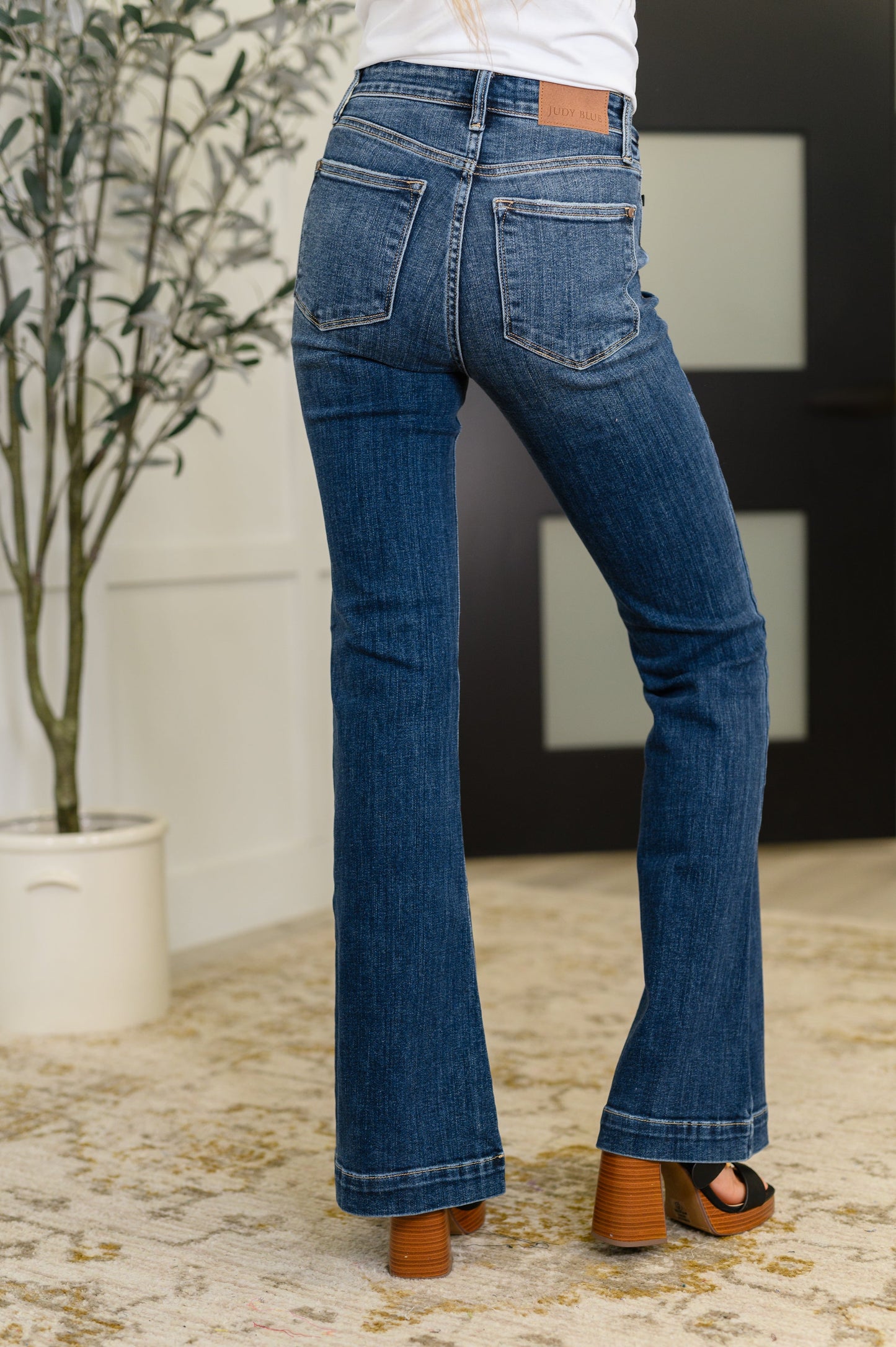 Person wearing blue jeans standing in a room with a plant and a black and white abstract painting.