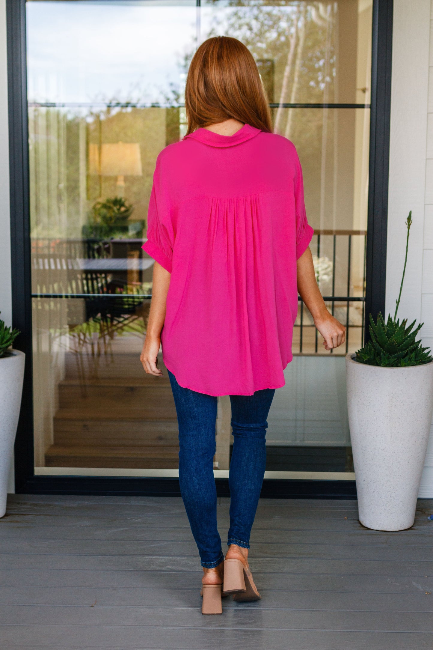 Woman wearing a bright pink top and blue jeans walking outside.