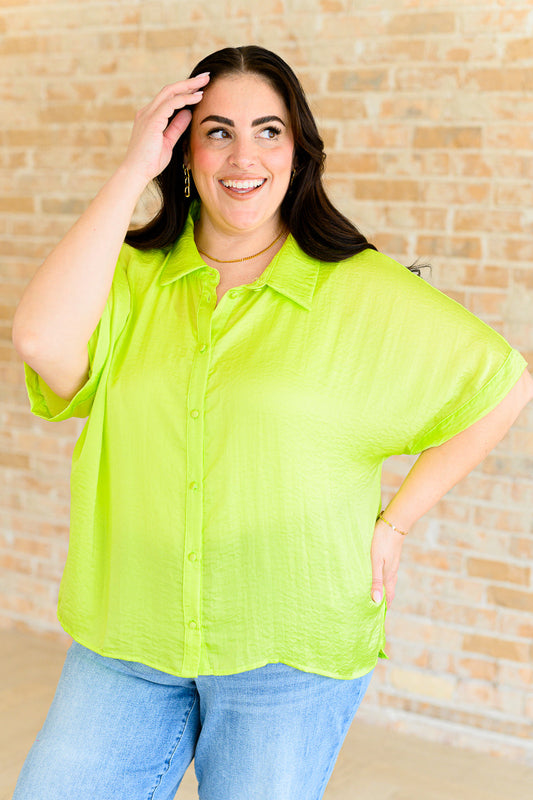 A plus size woman wearing a bright citrus yellow button down blouse with short sleeves, paired with a white top and blue jeans.