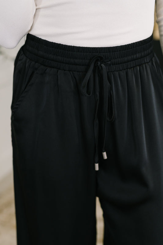 Black pants with drawstring waist worn by a person, blurred background