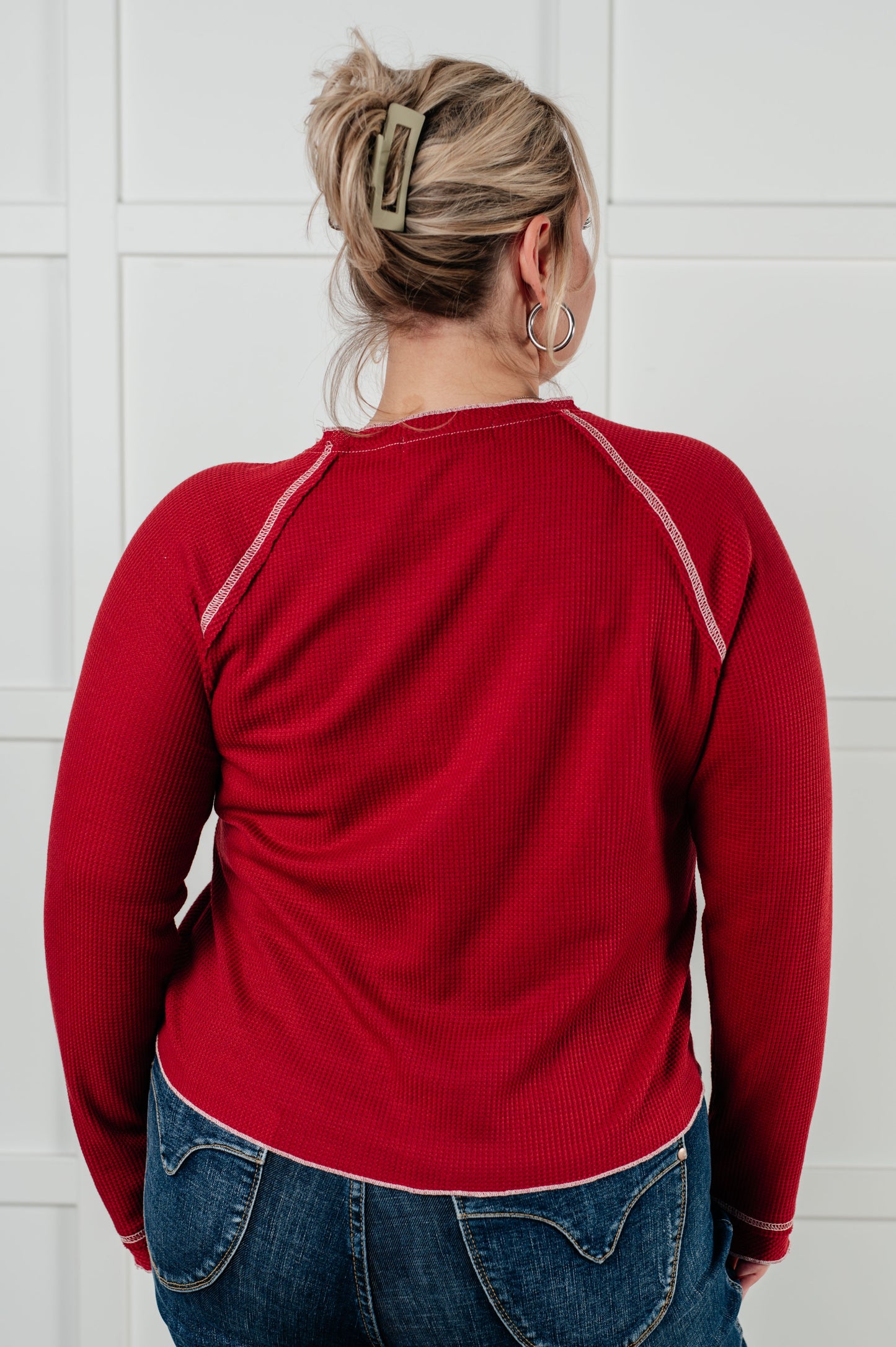 Person wearing a red long-sleeve shirt and blue jeans against a white tiled wall.