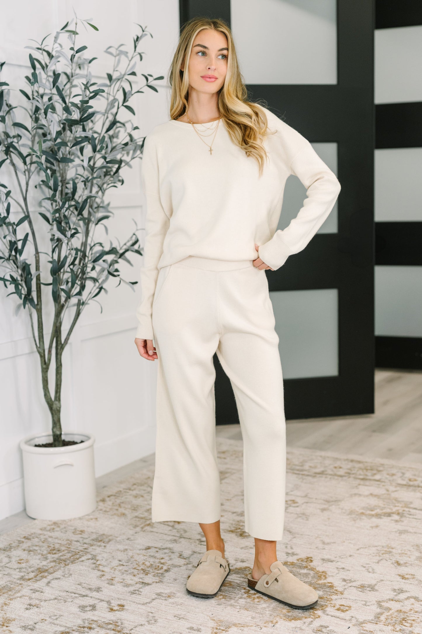Woman in a white outfit standing in a room with a plant and black and white wall.