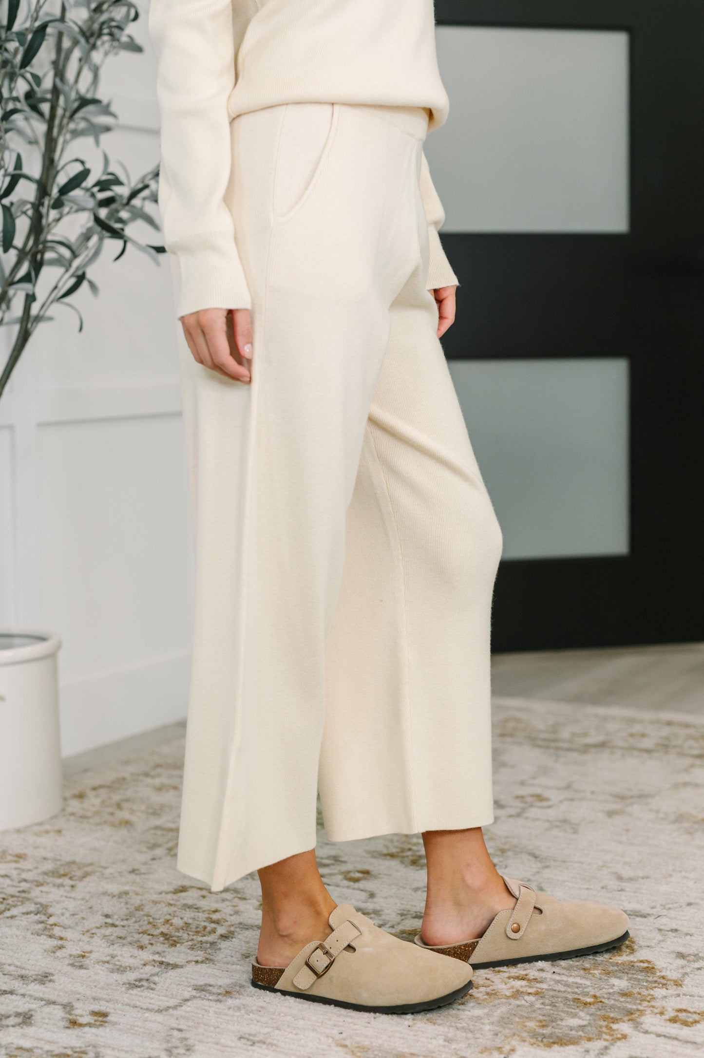 Person wearing a beige outfit with wide-leg pants and loafers indoors.