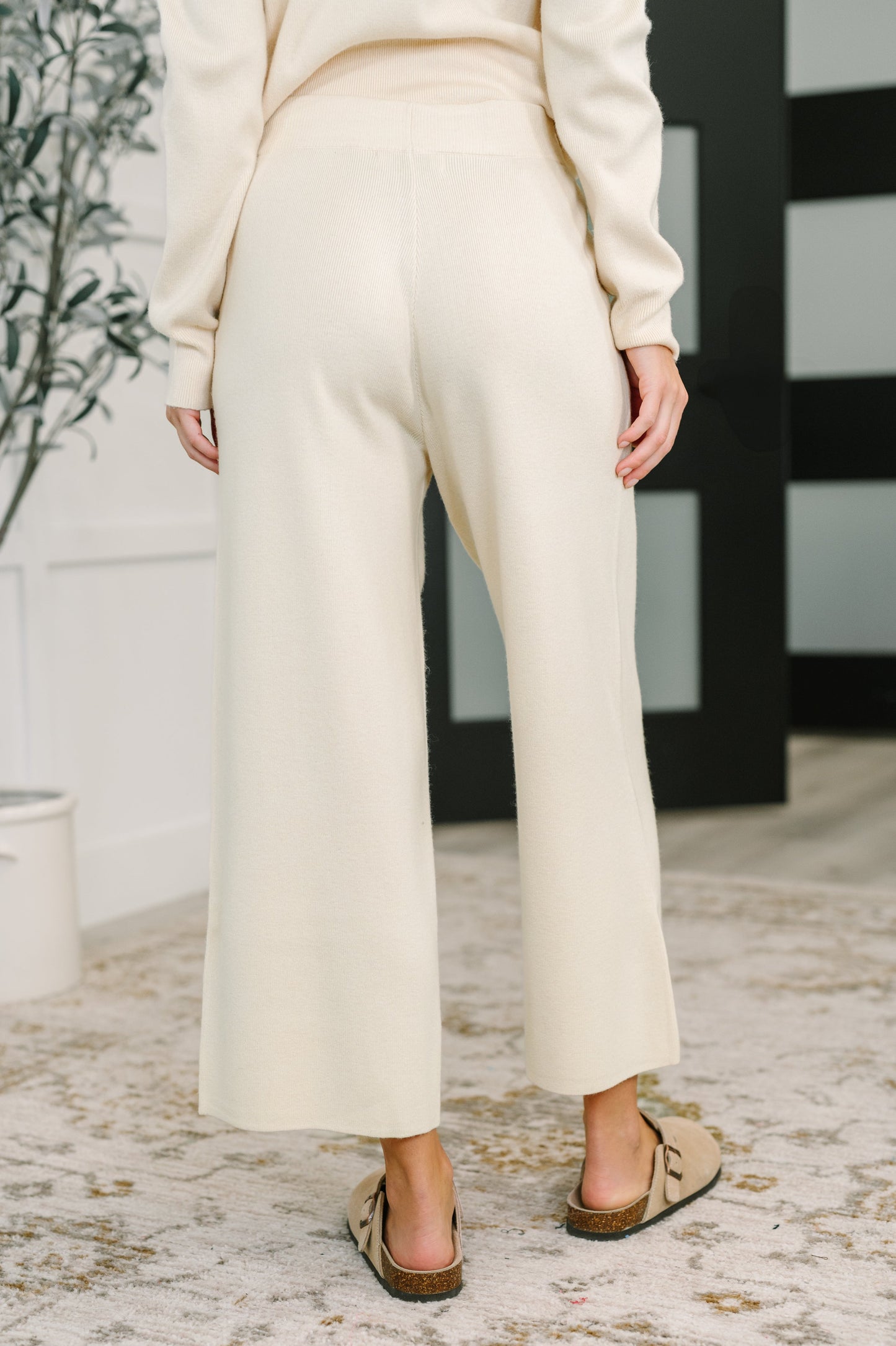 Person wearing a cream-colored outfit with wide-leg pants in an indoor setting.