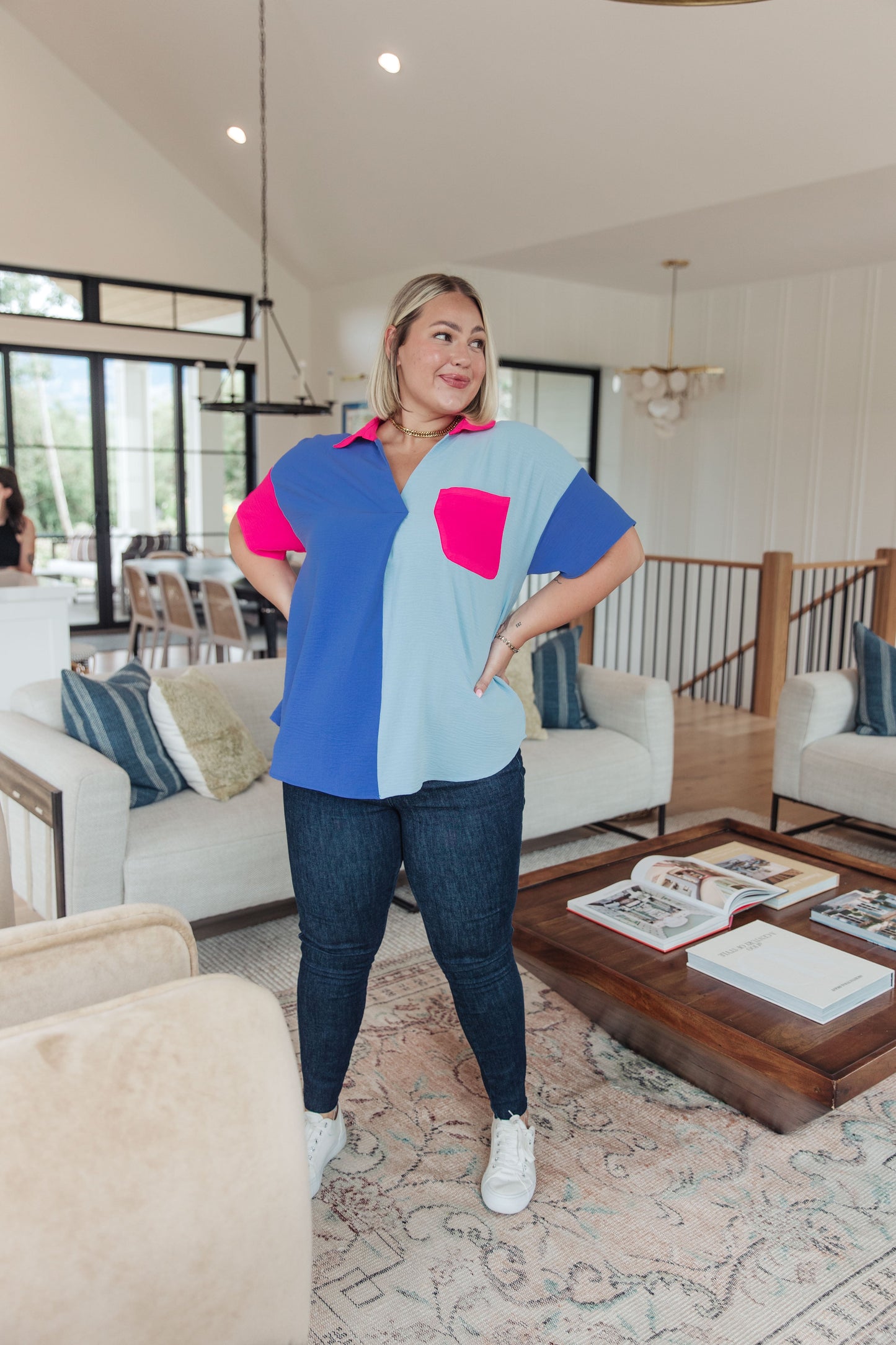 Woman standing in a modern living room wearing a colorful shirt and jeans.