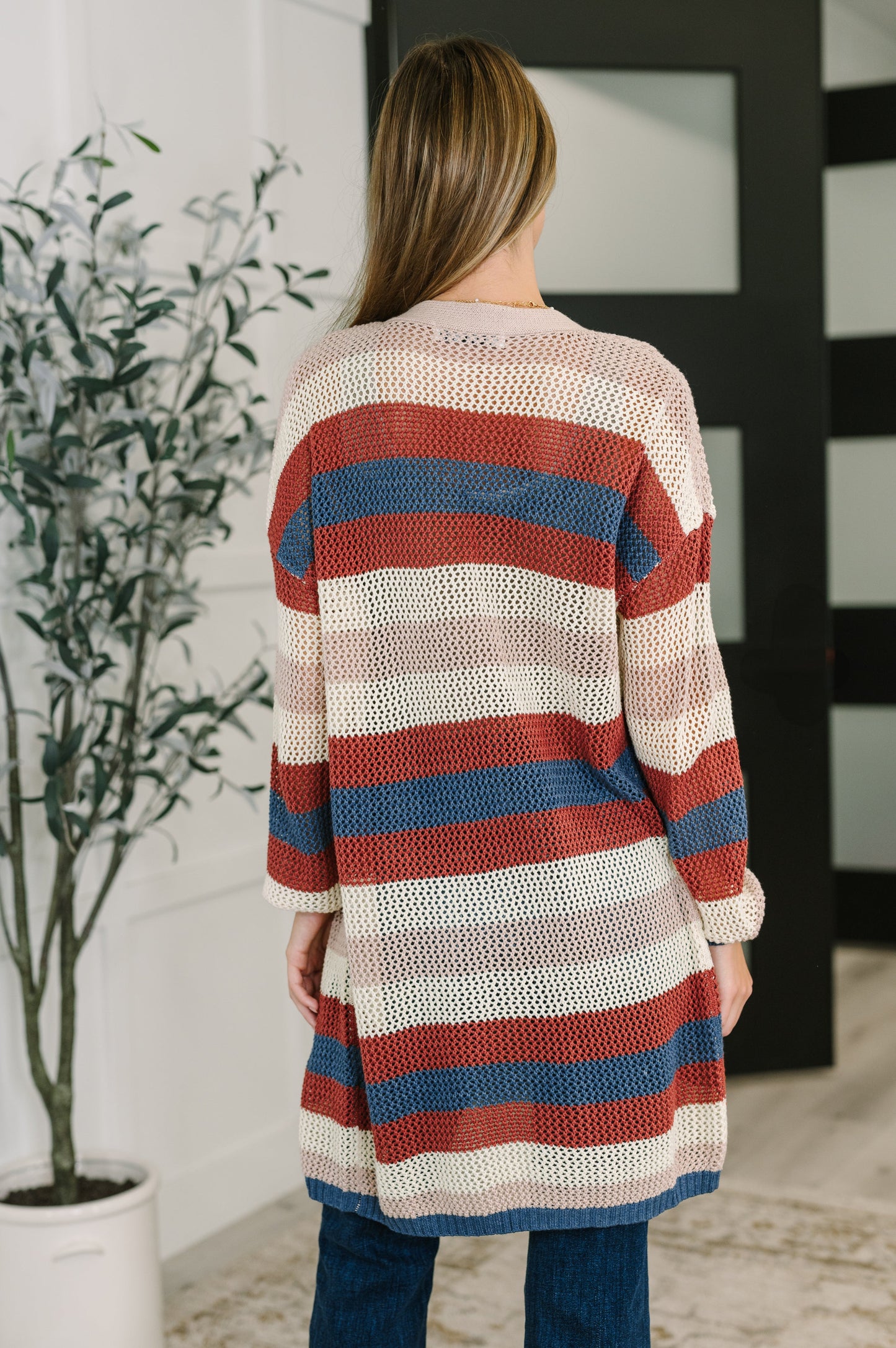 Person wearing a striped cardigan in a room with a plant and door in the background