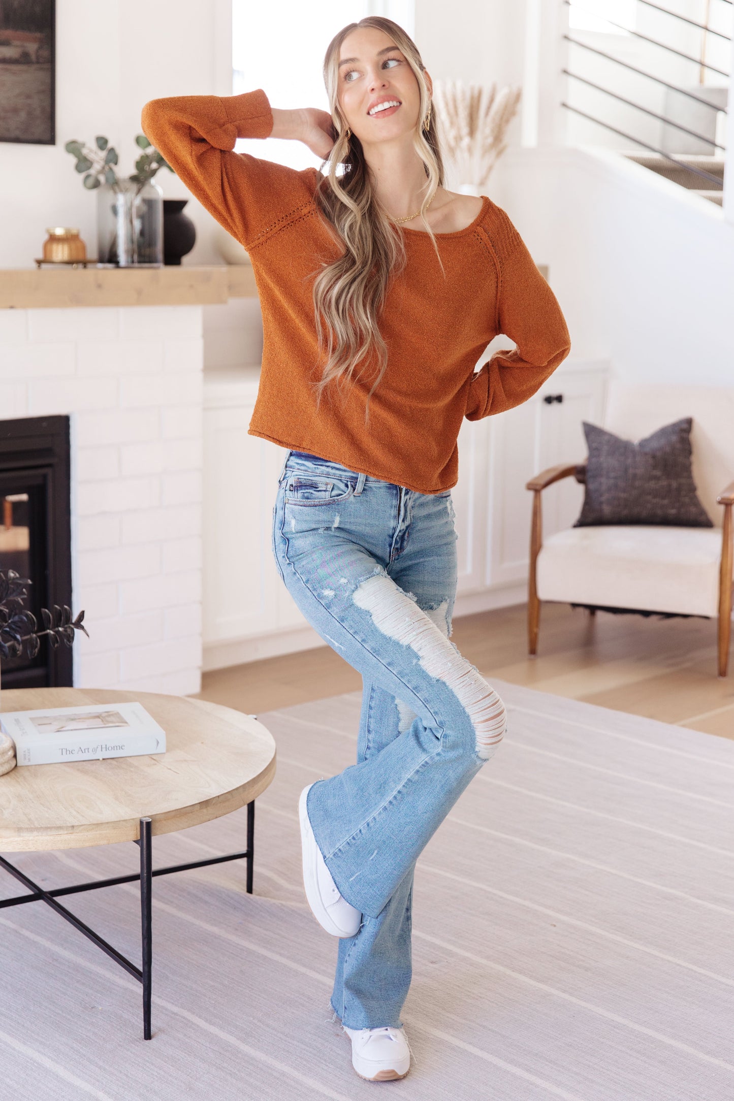 Woman in orange sweater and blue jeans standing in a living room.