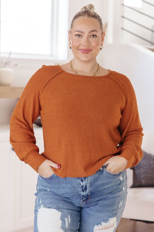 Woman wearing a rust-colored sweater and ripped jeans indoors.