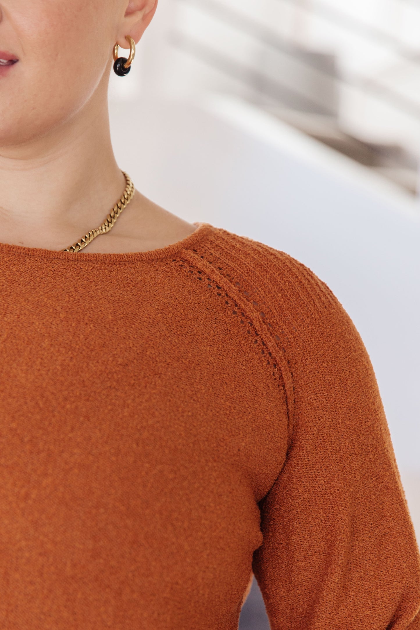 Close-up of a person wearing a rust-colored sweater with a blurred background