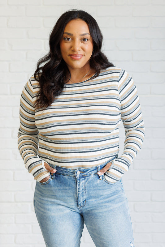 Woman wearing a striped sweater and jeans against a white brick wall