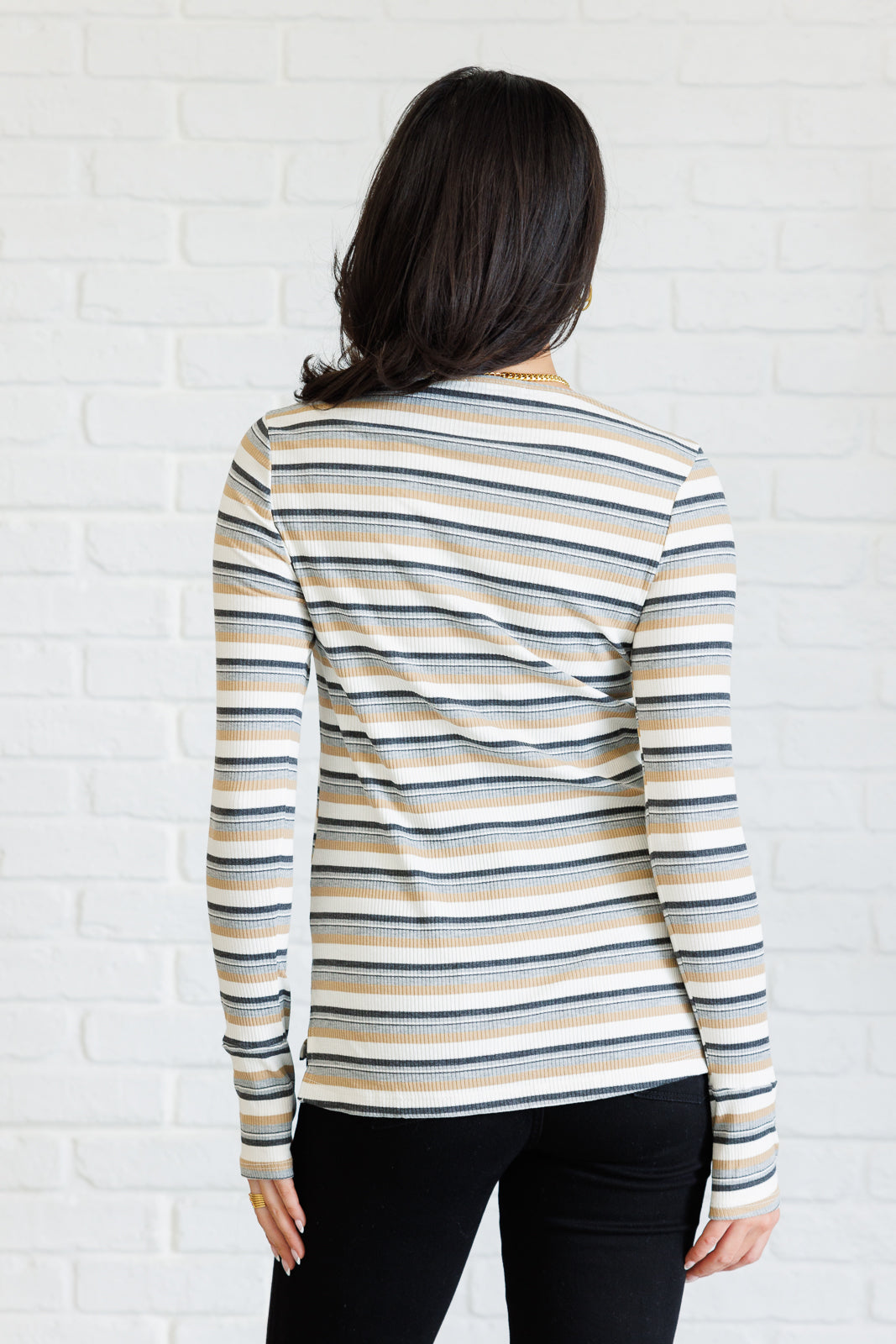 Woman wearing a striped long-sleeve shirt against a white brick wall.