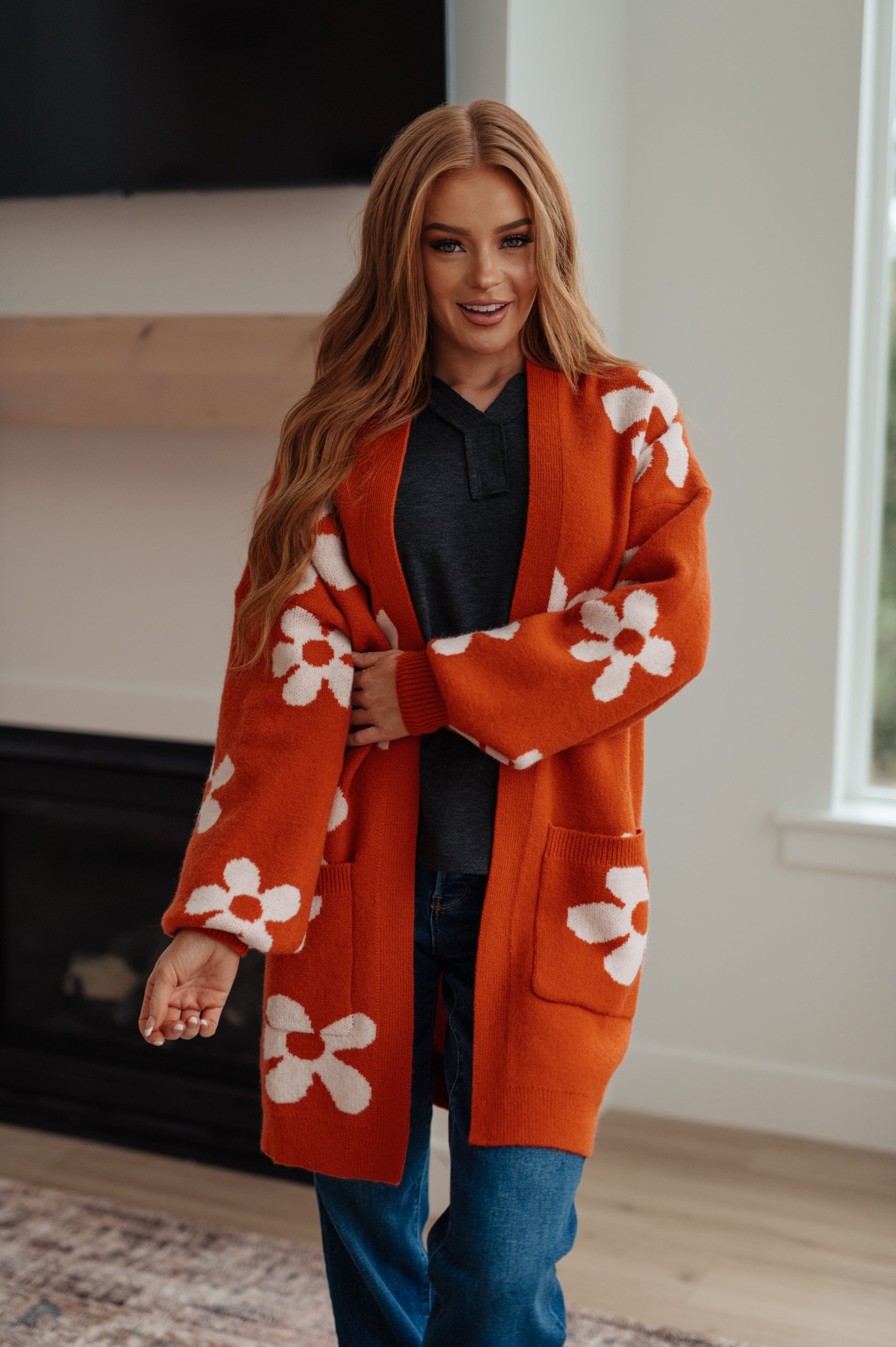 Woman wearing an orange cardigan with white floral patterns in a room.