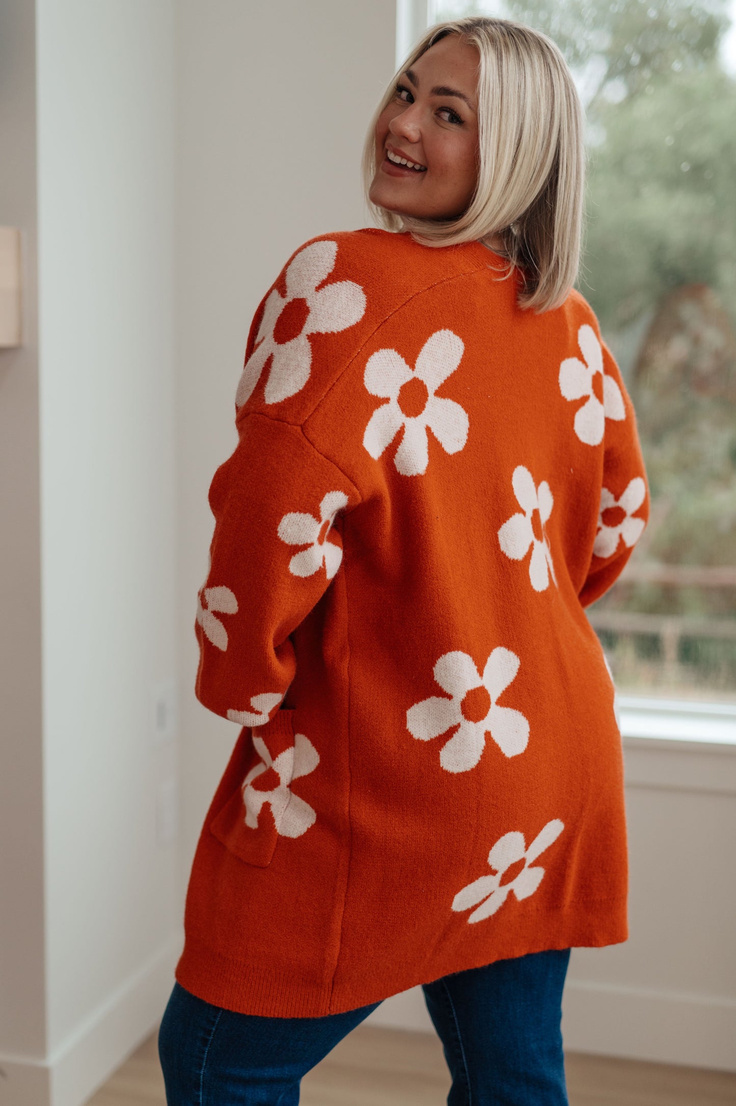 Person wearing an orange sweater with white floral patterns indoors.
