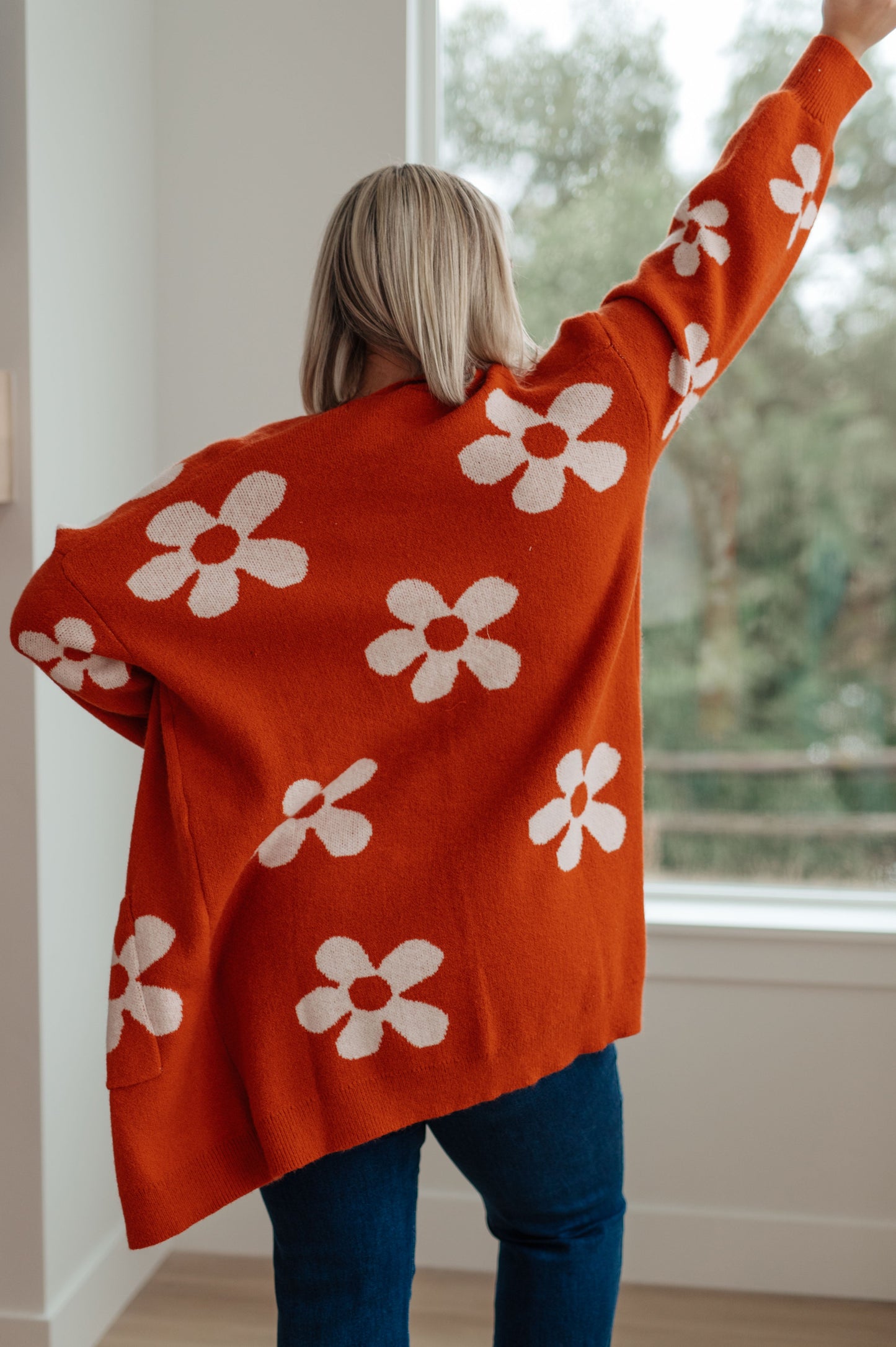 Person wearing an orange sweater with white floral patterns, standing indoors.